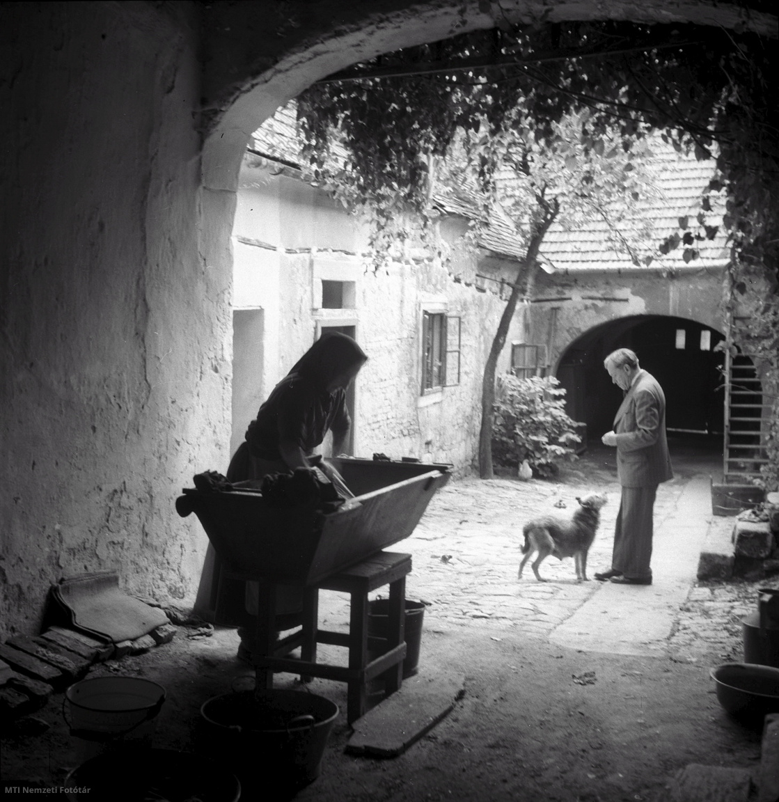 Sopron, 1956. június 16. Soproni asszony mos ruhákat egy régi ház udvarán. A háttérben egy ember kutyával.
