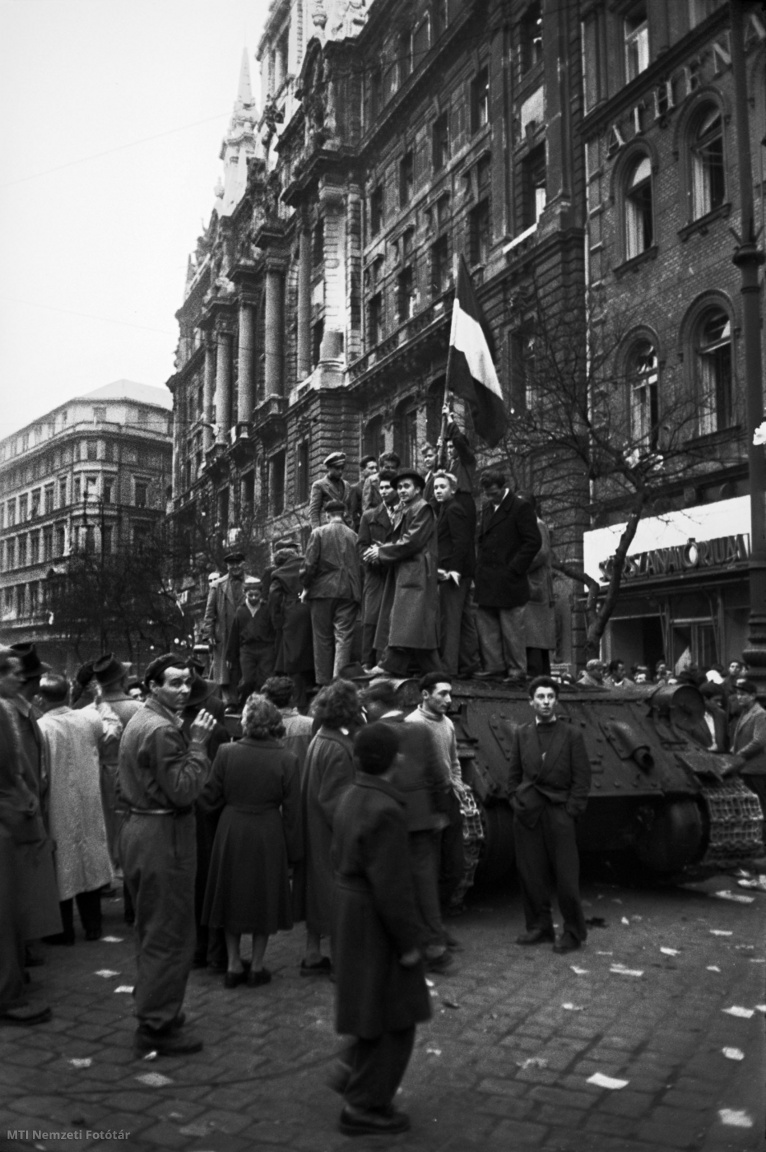 Budapest, 1956. október 25. Nemzeti zászlót lengető felkelők kapaszkodnak fel egy zsákmányul ejtett szovjet harckocsi tetejére a Lenin körúton (ma: Erzsébet körút) lévő New York Palota előtt, a Blaha Lujza tér környékén