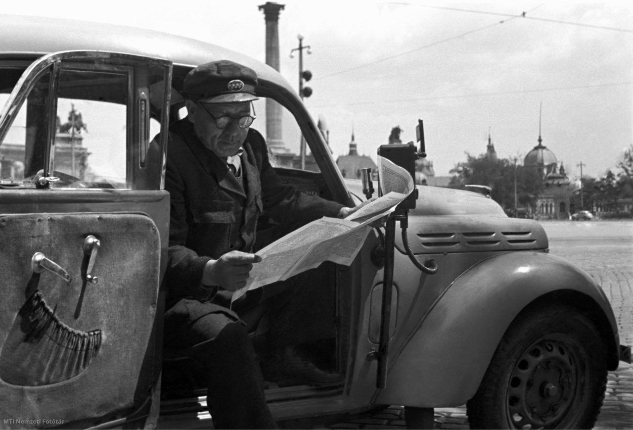 Budapest, 1952. május 15. Futó Sándor sztahanovista gépkocsivezető a taxi gépkocsijának ülésén olvas, nyitott ajtó mellett a Dózsa György úton. Hátul a Hősök terének egy részlete látható.