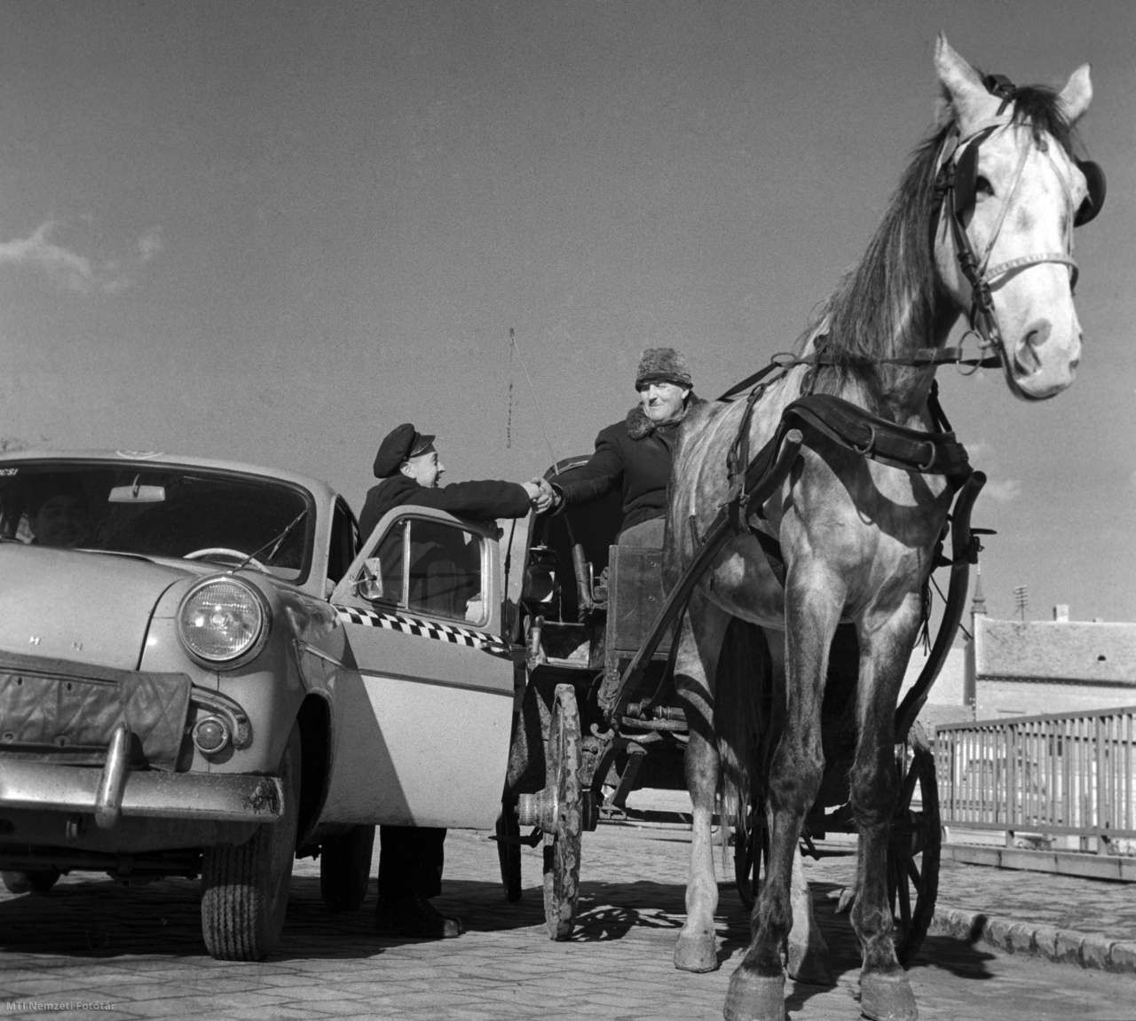 Baja, 1961. február 3. A konflis kocsisa kezet fog egy taxisofőrrel Baján. Az új közlekedési fajták szinte teljesen kiszorítják a régi konflisokat.