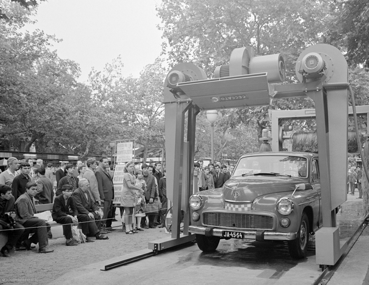 Budapest, 1968. május 19. Sokan figyelik az olasz Ceccato cég önműködő gépkocsimosójában tisztuló taxit a Budapesti Nemzetközi Vásáron. A Pietro Ceccato által alapított cég eredetileg kenyérgyári gázégőket gyártott, később levegőkompresszorokat és javítóállomások berendezéseit. 1956 után jelentek meg a garázsfelszerelések és gépkocsimosók piacán. A Warszawa M201-es taxi hűtőmaszkjában lévő nyílás a kurbli helye.