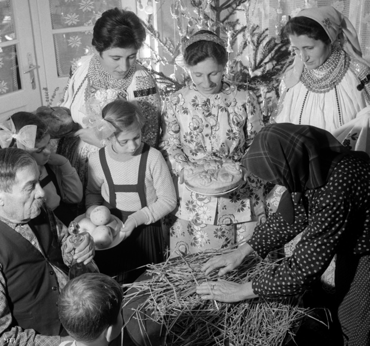 Egy sokác család legidősebb tagja szalmát tesz a terítő alá hogy azon fogyasszák el a karácsonyi vacsorát 1964-ben.