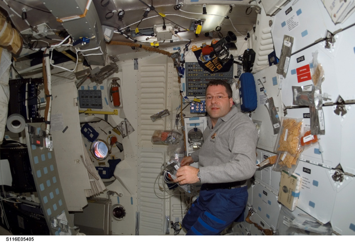 Nicholas J. M. Patrick, az STS-116 küldetésspecialistája a Discovery középfedélzetén található tárolórekeszekből készíti elő a legénység étkezését. A kép bal oldalán jól látható az átalakított, tépőzárral a falhoz rögzített iPod, és hangszórók.