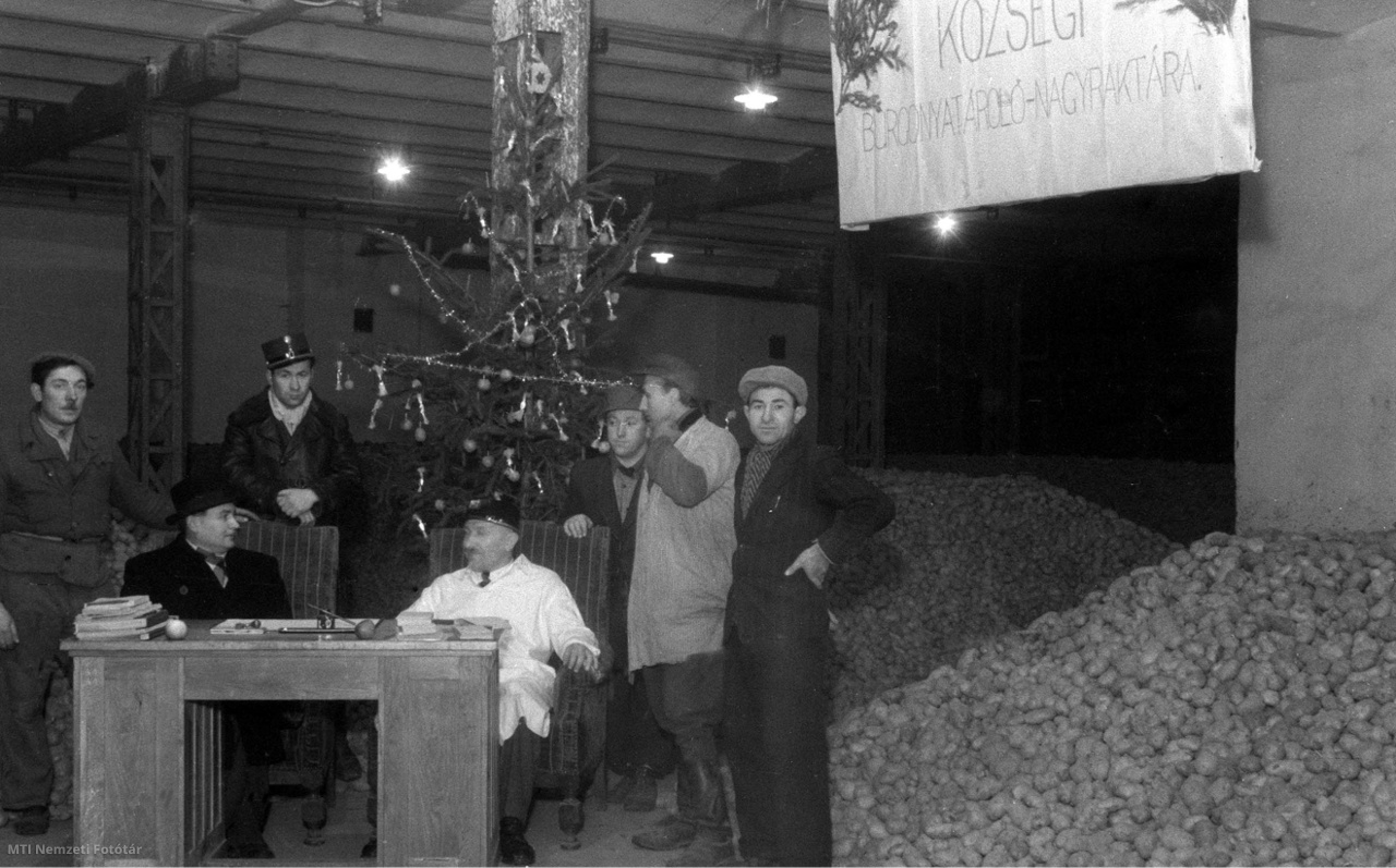 Budapest, 1946. december 23. Burgonyahalmok előtt álló asztalnál várják a rászorulókat a fővárosi Községi Élelmiszerkereskedelmi Rt. (KÖZÉRT) burgonyaraktárában, ahol a budapesti lakosság számára karácsonyi burgonyaosztási akciót tartanak.