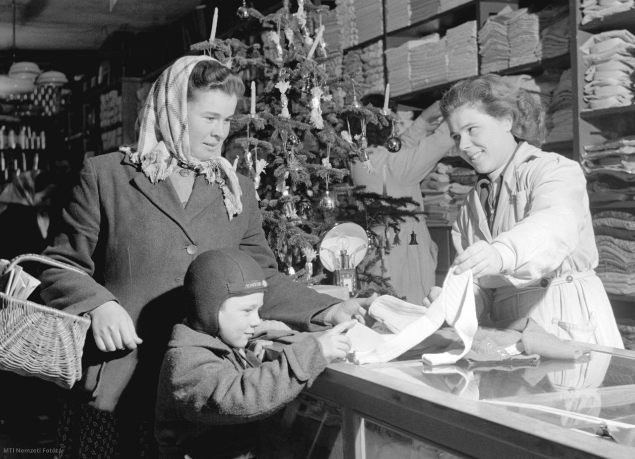 Pásztó, 1955. december 14. Kiss Erzsébet eladó (j1) kötött gyermekpulóvert mutat Dávid Gyulánénak és kisfiának a Pásztói Földműves-szövetkezet Kisáruházának karácsonyi vásárán. 