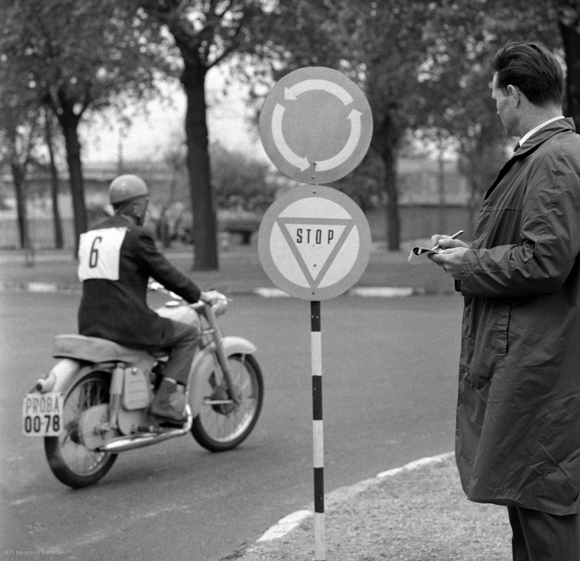 Budapest, 1965. május 21. Vizsgázó motorkerékpáros jelzőtáblákra való reagálását figyeli a vizsgabizottság tagja a népligeti vizsgapályán. A motorkerékpárosok eddig az elméleti vizsgák után csak igen egyszerű, ún. biztonsági feladatot oldottak meg a vizsgán. A KPM Autóközlekedési tanintézet új vizsgarendszerén egy 2 km-es vizsgapályán kell áthaladniuk. Ezen az útszakaszon megtalálhatók mindazok az útelemek, amelyek a közlekedésben a legfontosabbak. A vizsgabizottság figyeli a motorkerékpáros reagálását a jelzőtáblák és egyéb útelemek észlelésekor és csak jól képzett vezetőket engednek részt venni a forgalomban.