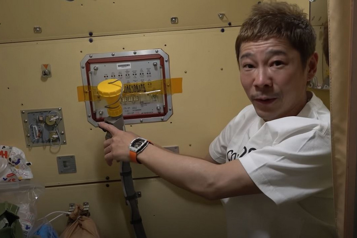 Maezava éppen azt a csövet mutatja, melyen keresztül vizelni lehet a Nemzetközi Űrállomáson