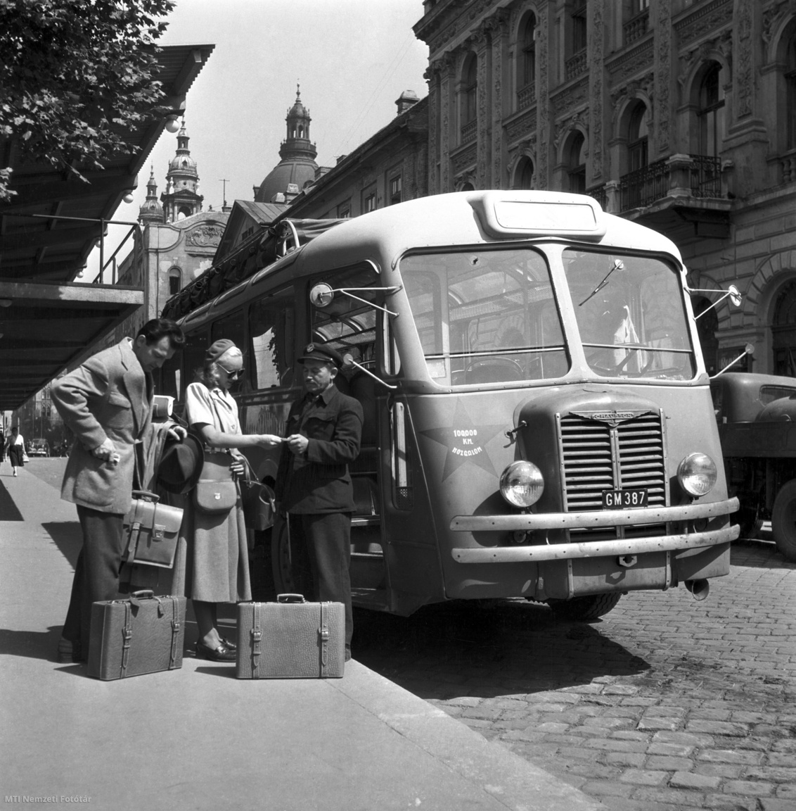Budapest, 1950. augusztus 1. A buszvezető ellenőrzi a bőröndökkel, retiküllel utazó pár menetjegyét felszállás előtt egy Chausson típusú autóbusznál a Sztálin téri buszpályaudvaron, a Tanninpex (volt Bőr- és Szőrme) Nemzeti Vállalat reklámfotóján. A háttérben a Szent István-bazilika kupolája és tornyai