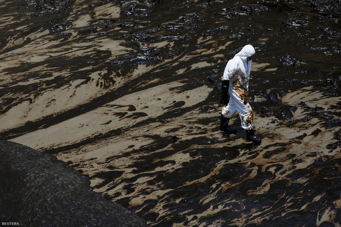 A munkások a vulkánkitörés által kiváltott hullámok okozta olajszennyezést takarítják