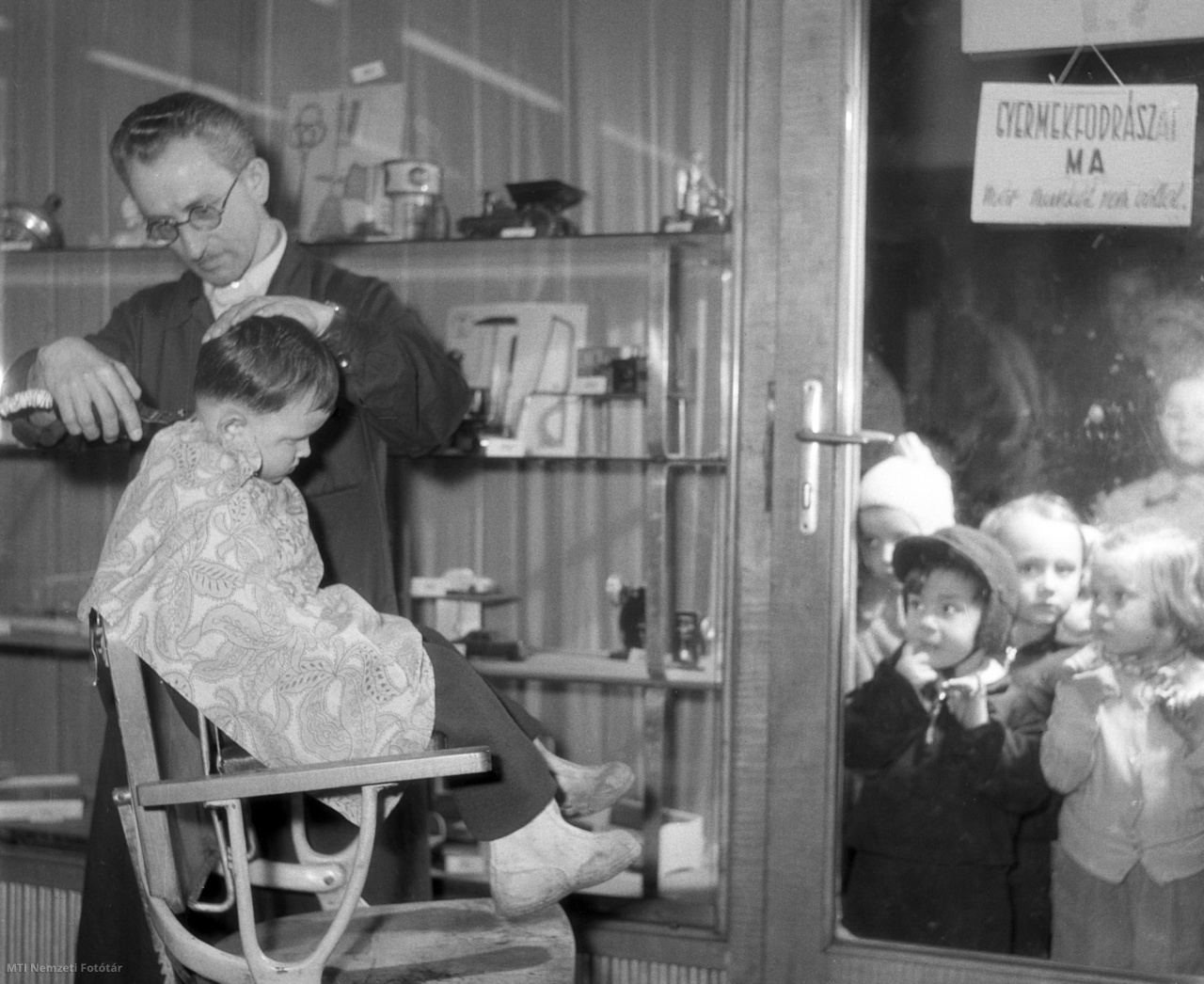 Budapest, 1957. február 4. Gyermekek nézik a kirakaton keresztül Ambró István fodrászt, aki egy gyermek haját vágja az Úttörő Áruházban működő gyerekfodrászatban