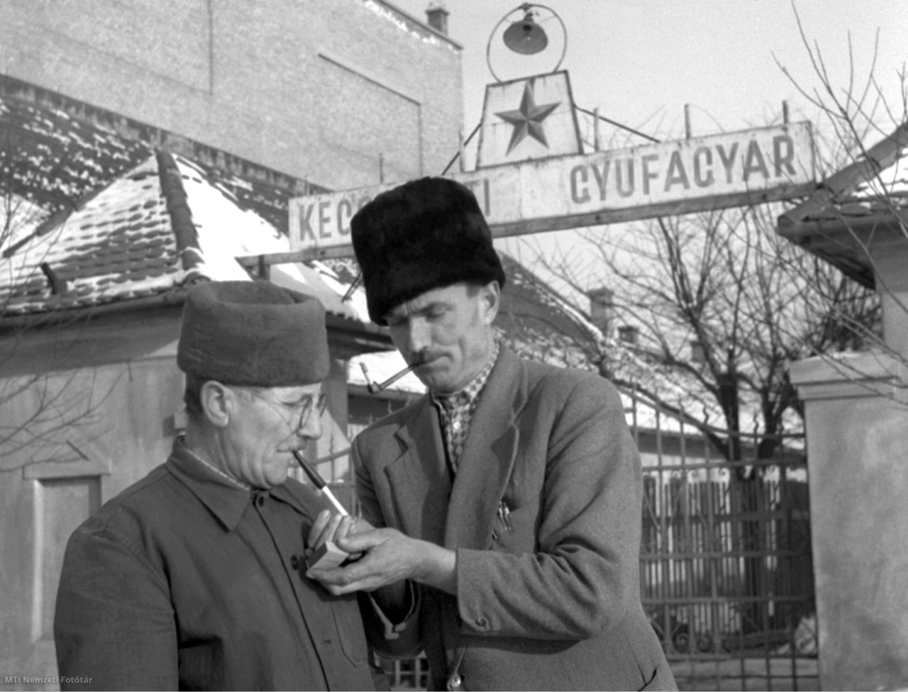 Kecskemét, 1956. február 5. A Kecskeméti Gyufagyár dolgozói pipára gyújtanak a gyárban készült gyufával az épületen kívül, a kapubejárat előtt.