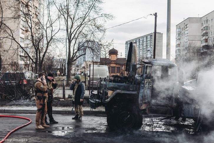 Ukrán katonák állnak a kiégett katonai járművük mellett 2022. február 25-én Kijevben
