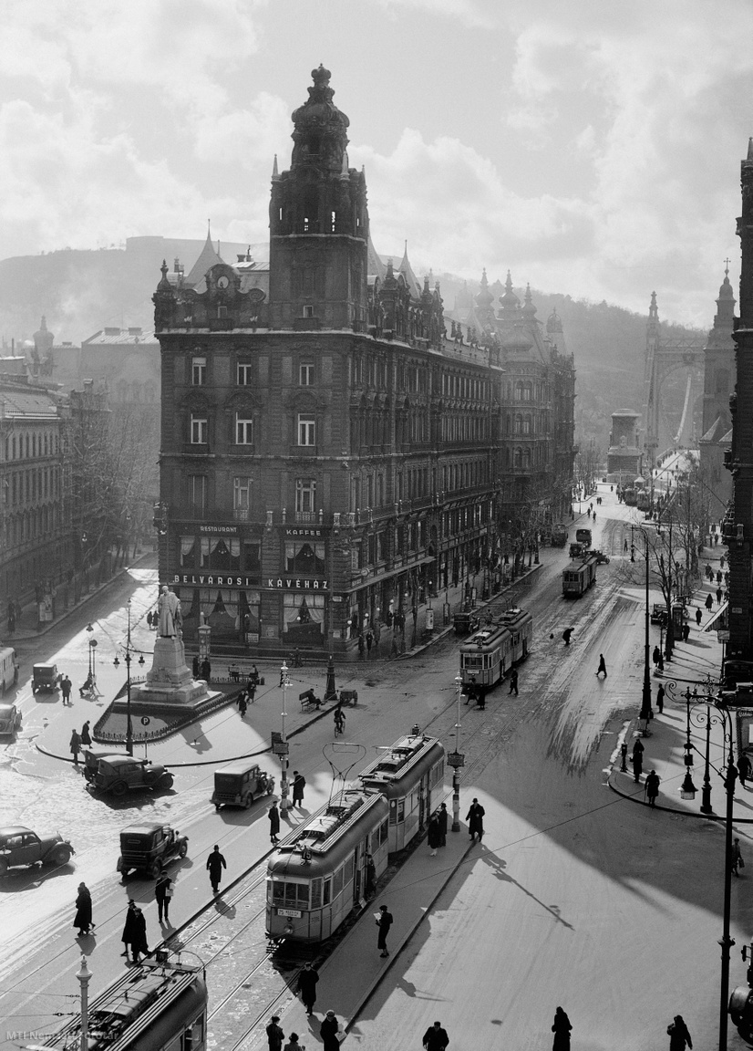 Budapest, 1930s Pest part of the city: the southern Klotild Palace on the ground floor at the Pest end of the Elizabeth Bridge, on the ground floor, and the statue of István Werbőczy in front of the building.  Trams passing by the Free Press next to the Klotild Palace carry passengers, and in the background you can see the outlines of Gellért Hill in Buda.  The exact time of recording is unknown.