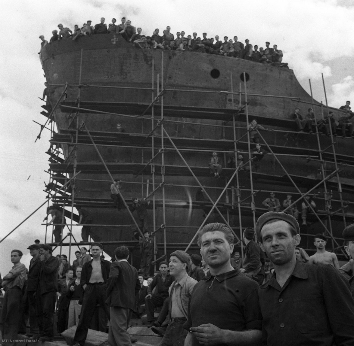 Budapest, 1959. szeptember 1. A Gh. Dej Hajógyár dolgozói vállalták, hogy a pártkongresszus tiszteletére 12 hónap alatt két új típusú, 1200 tonnás Duna-tengerjáró hajót készítenek el. Az első hajót a vállalásnak megfelelően, szeptember 1-jén bocsátották vízre. A képen: a hajógyár munkásai a vízre bocsátáson, mögöttük a második hajó, amelyet december végén fejeznek be
