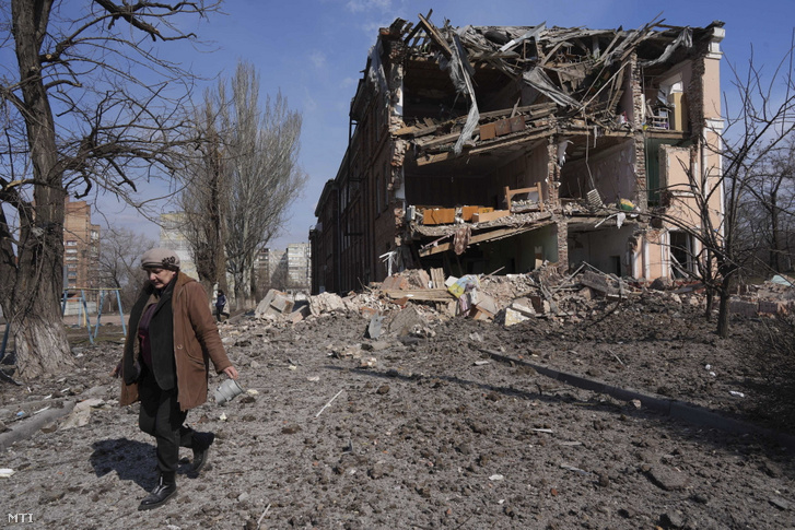 Egy nő halad el egy tüzérségi támadásban megrongálódott épület előtt Mariupolban 2022. március 13-án