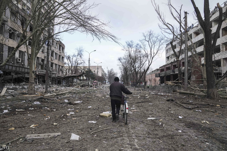 Megrongálódott lakóépületek romjai között tolja kerékpárját egy férfi a délkelet-ukrajnai Mariupolban 2022. március 10-én