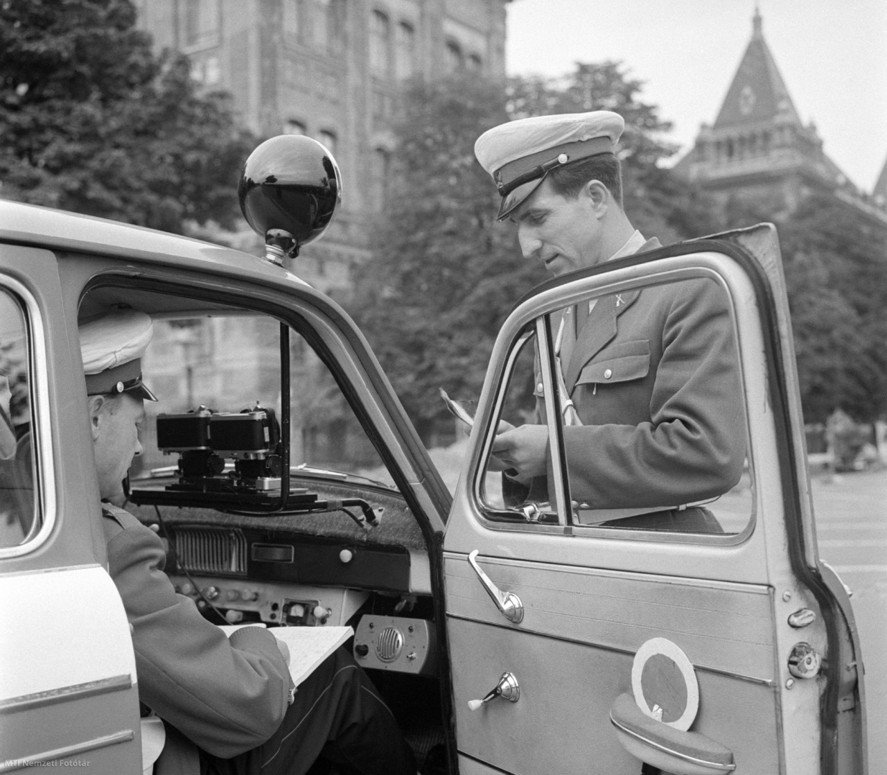 Budapest, 1965. augusztus 27. Rendőrautóba szerelt, fényképezőgépekkel kombinált közúti sebességmérő műszerrel (traffipax) ellenőrzik a Közlekedésrendészet közúti ellenőrző csoportjának tagjai a közúti közlekedést a Műegyetem rakparton. A berendezés fényképeken regisztrálja a gyorshajtást. A fotón nemcsak a gépkocsit és rendszámát, hanem a napi dátumot, az órát és kilométer/órában a sebességet is rögzítik.