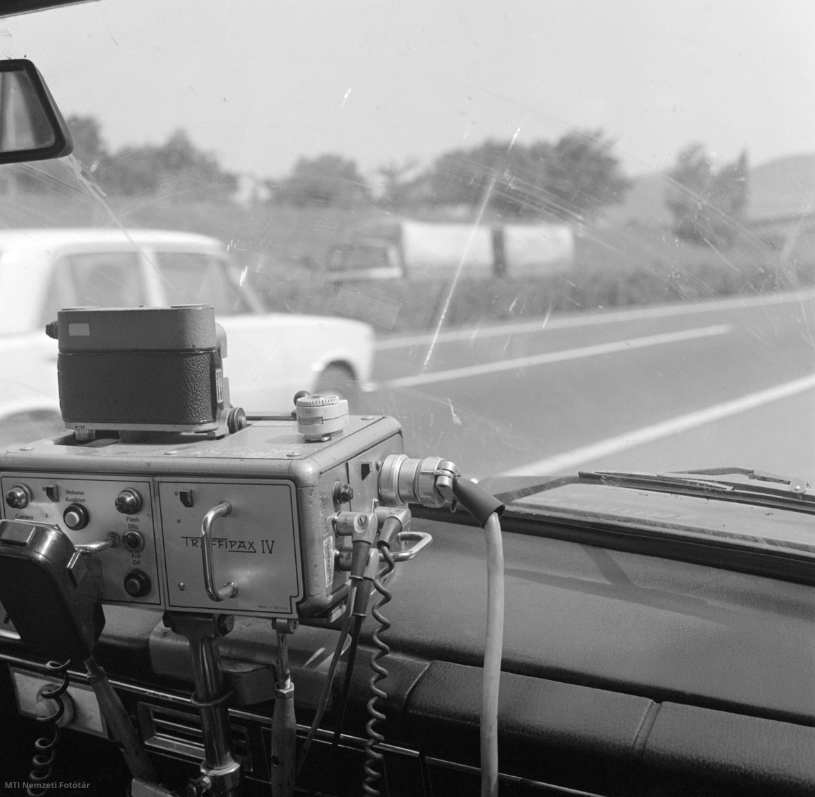 1981. június 13. Microspeed gyártmányú traffipax berendezés fényképezi a gyorshajtókat, egy rendőrségi autó utasteréből, az M7-es autópályán. 1967-ben jelent meg Magyarországon az első traffipax. Pár év múlva kerültek a rendszerbe a német gyártmányú Microspeed, majd a Speedophot traffipaxok, amelyek pontosabbak voltak elődeiknél. Működési elvük: a sebességet a Doppler-elv alapján számították ki, vagyis mérték, hogy a rádióhullámok miként változnak meg a kocsikról visszaverődve.