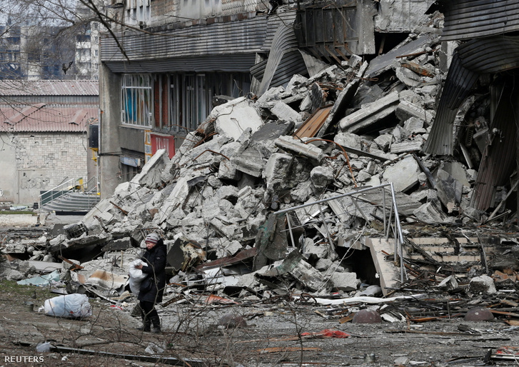 Egy helyi lakos egy zsákot cipel egy lerombolt mariupoli bérház közelében 2022. március 31-én