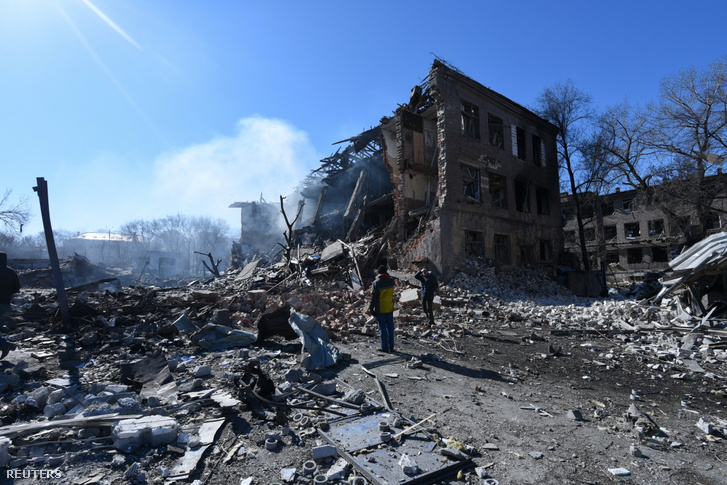 Emberek állnak egy lerombolt cipőgyár előtt egy rakétatámadást követően Dnyipróban, Ukrajnában 2022. március 12-én