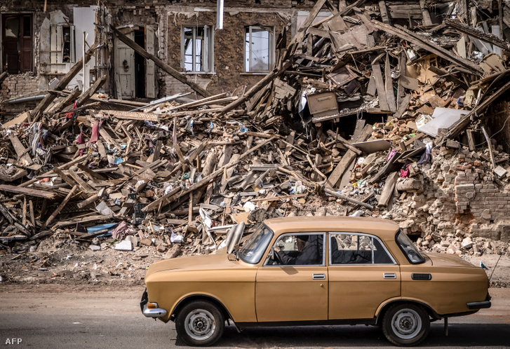 Egy férfi elhajtott egy autóval egy lerombolt épület romjai mellett a kelet-ukrajnai Harkiv városában 2022. április 2-án