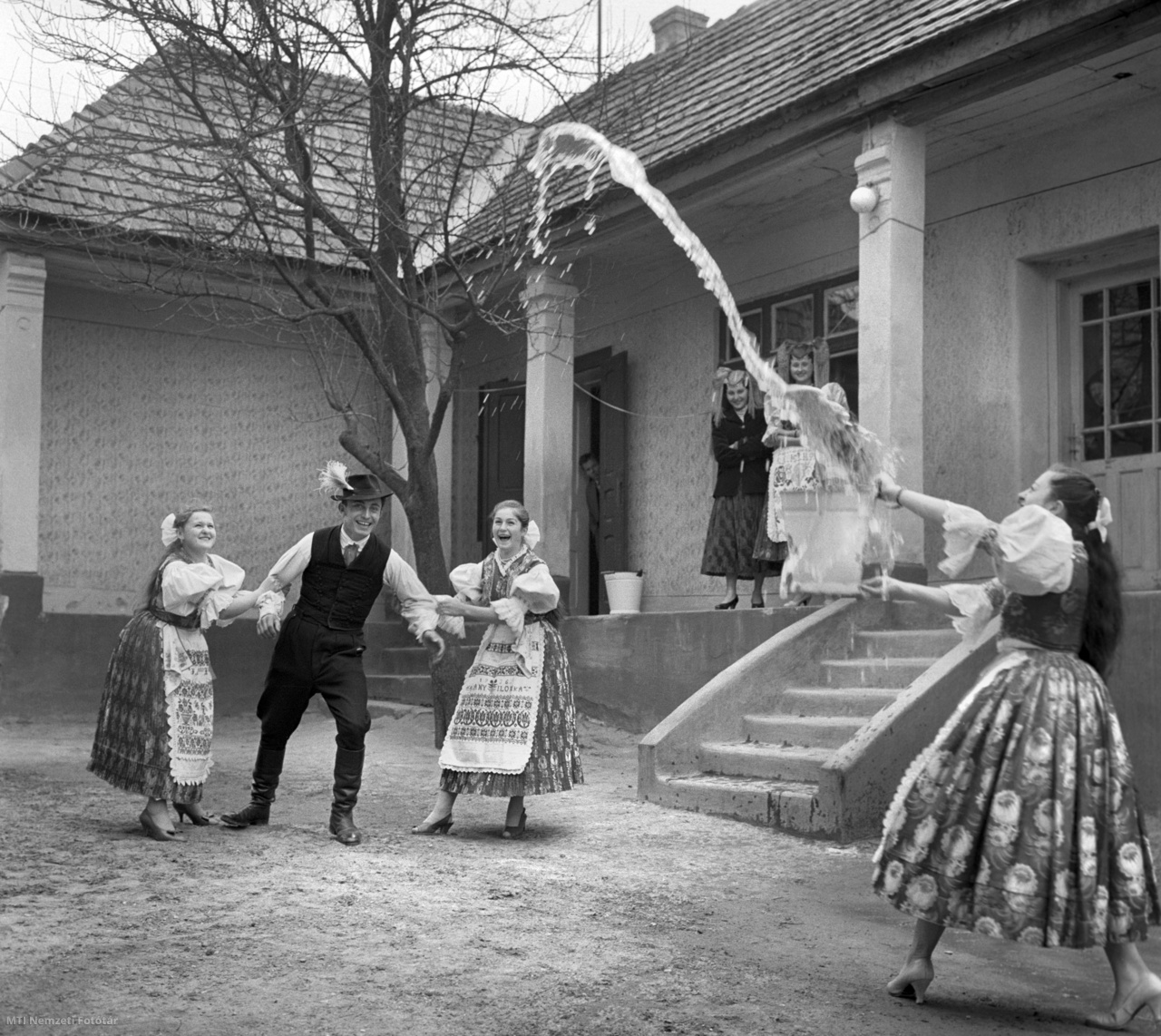 Őrhalom, 1961. március 31. Egy legényt fog le két lány húsvét keddjén Őrhalmon, miközben társuk a település hagyományait követve meglocsolja egy vödör kútvízzel.