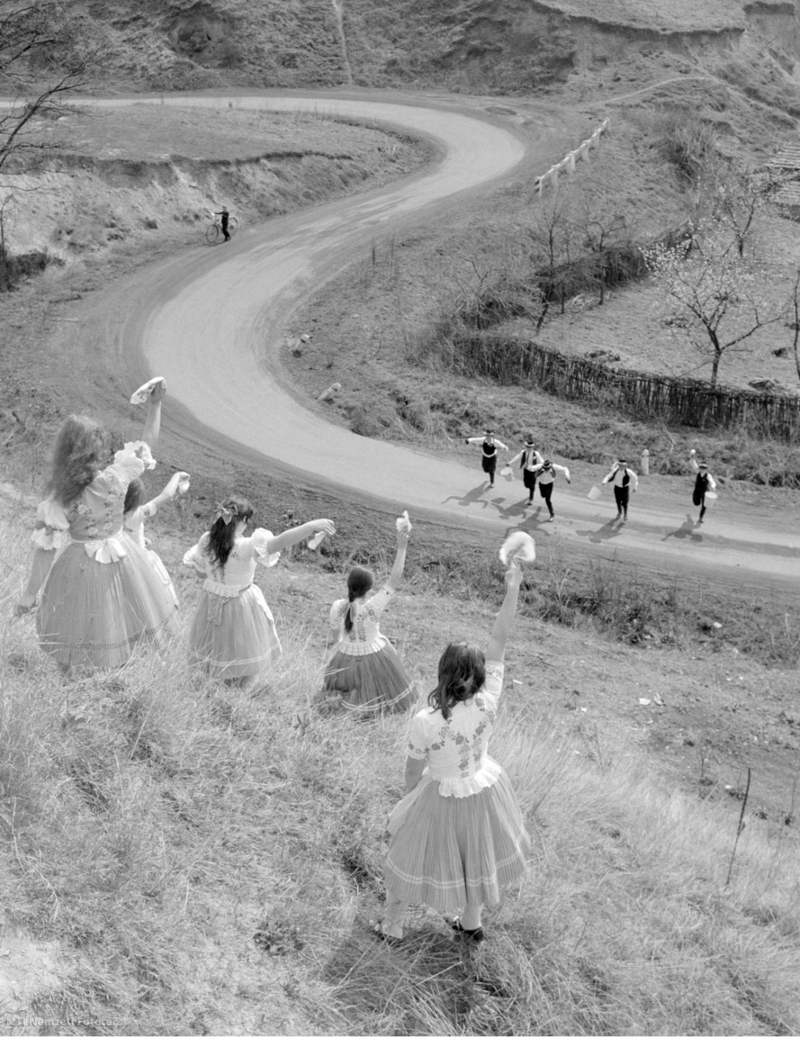 Szente, 1971. április 12. Ünnepi palóc népviseletbe öltözött lányok keszkenőjükkel integetnek a dombtetőről a locsoló legényeknek. A Nógrád megyei faluban még él az eredeti húsvéti népszokás, hogy nem kölnivízzel öntözik a lányokat.