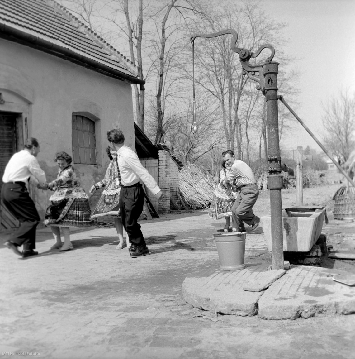 Sióagárd, 1959. március 30. A férfiak a kerti kúthoz húzzák a népviseletbe öltözött lányokat, hogy a húsvéti hagyományoknak megfelelően meglocsolják őket friss vízzel.