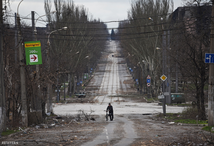 Egy helyi lakos kerékpárral sétál az utcán Mariupolban 2022. április 4-én