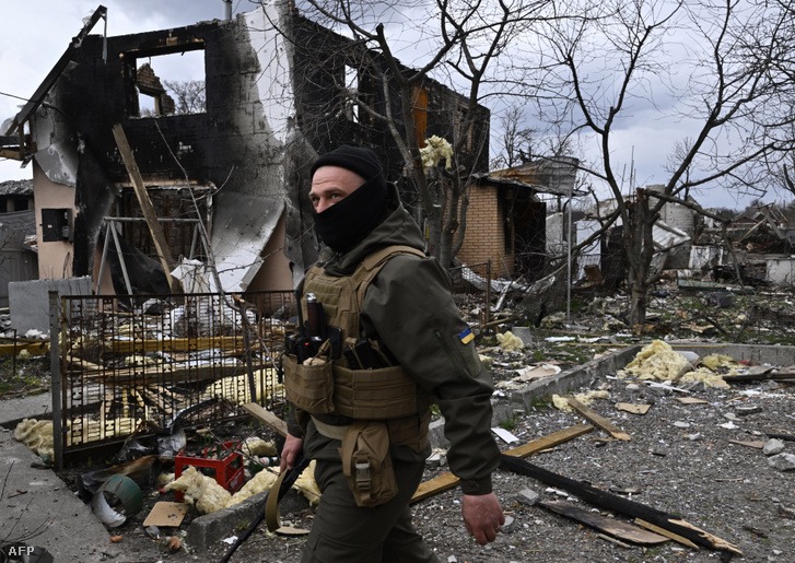 Az ukrán területi védelmi erők egyik tagja egy lerombolt ház előtt sétál 2022. április 12-én