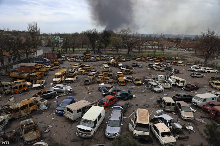 Megrongálódott és kiégett járművek az Iljics Acél- és Vasművek területén, miközben füst száll fel az Azovsztal acélgyár területéről Mariupolban 2022. április 18-án