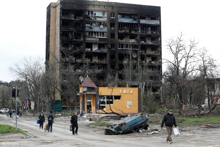 Helyi lakosok sétálnak el egy leégett épület mellett Mariupolban, Ukrajna déli kikötővárosában 2022. április 21-én