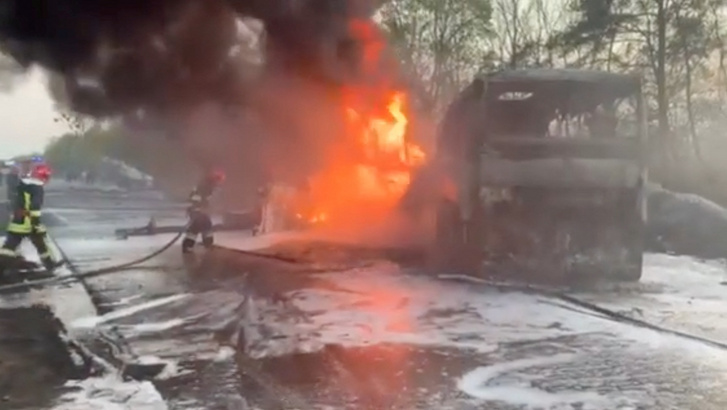 Tűzoltók vizet permeteznek egy kigyulladt járműre, miután egy üzemanyagszállító teherautó összeütközött egy autóbusszal Szitne település térségében, Ukrajnában 2022. május 3-án