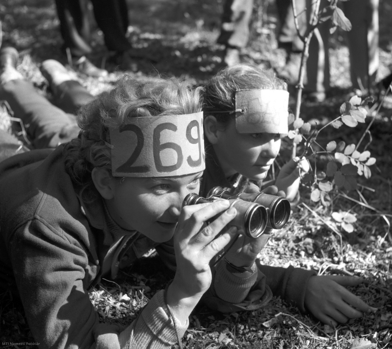 Sárbogárd, 1957. október 6. Sélley Erzsébet, a sárbogárdi általános iskola tanárnője távcső segítségével próbálja leolvasni az ellenfelek számait a sárbogárdi járási úttörők nagy őszi számháborúján a vajtai erdőben.