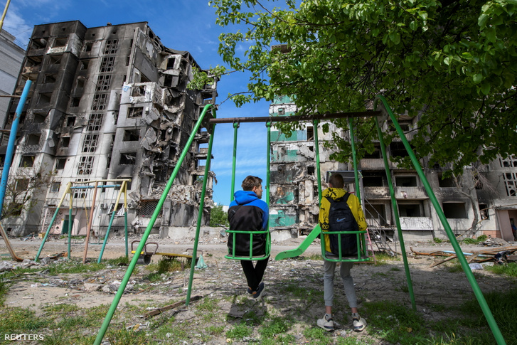 Fiatalok hintáznak egy lebombázott lakóépületek előtt Borodianka városában Ukrajnában 2022. május 13-án