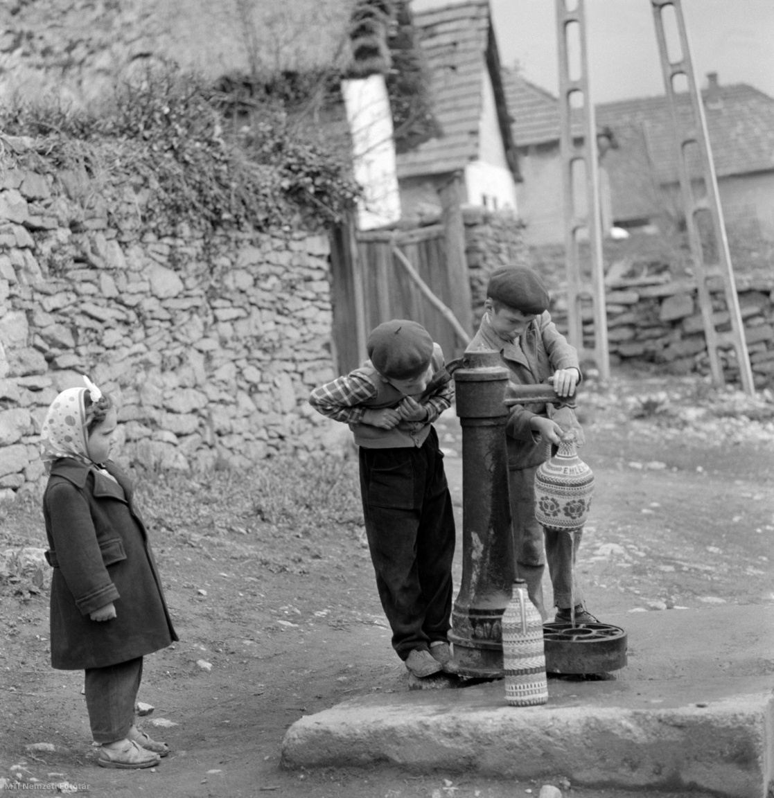 Magyarország, 1964. április 27. Fiúk egy utcai nyomókúton – Norton kút – vízzel töltik meg a demizsonokat, miközben egy kislány figyeli őket. A felvétel készítésének pontos helye ismeretlen