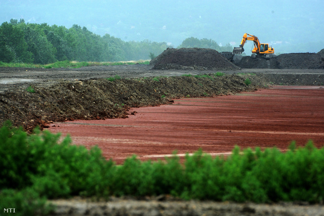 A már feltöltött területen növények telepedtek meg 2012-ben. A háttérben a Tatai Környezetvédelmi Zrt. (TKV) munkagépe mesterséges talajjal fedi be a volt Almásfüzitői Timföldgyár vörösiszap-tározóját.