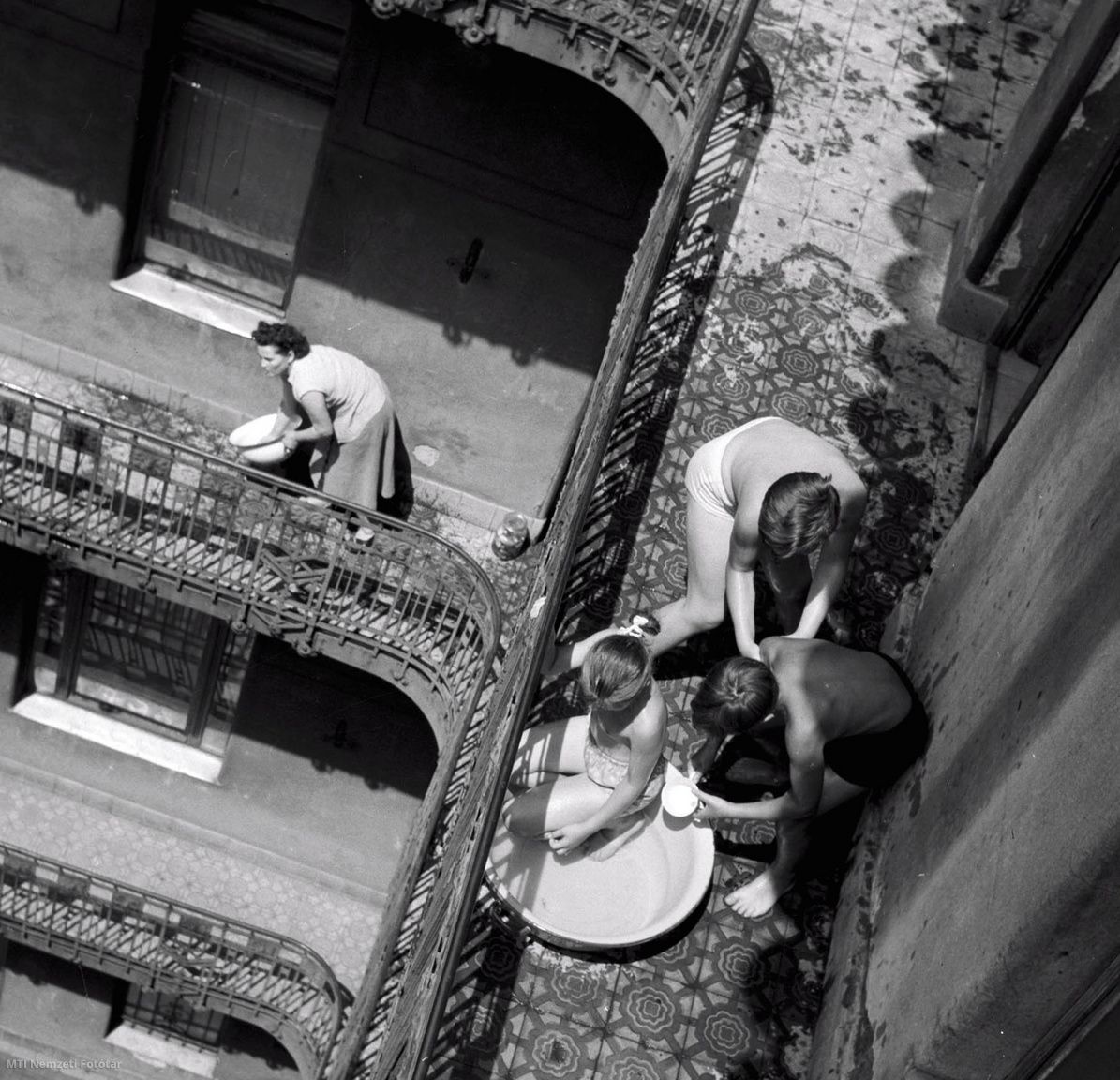 Budapest, 1957. július 9. Kánikulában az erzsébetvárosi Elemér utca 31. számú bérház függőfolyosóján lavorból magukat hűsítő gyerekek. 