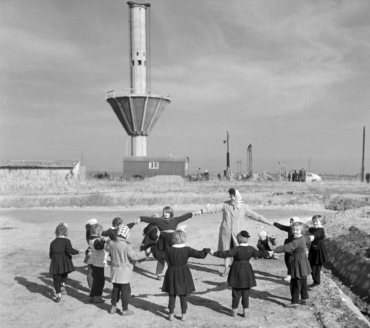 Aszód, 1961. november 1. Iskolás gyerekek tanítónőjükkel körjátékot játszanak az épülő víztorony közelében Aszódon.