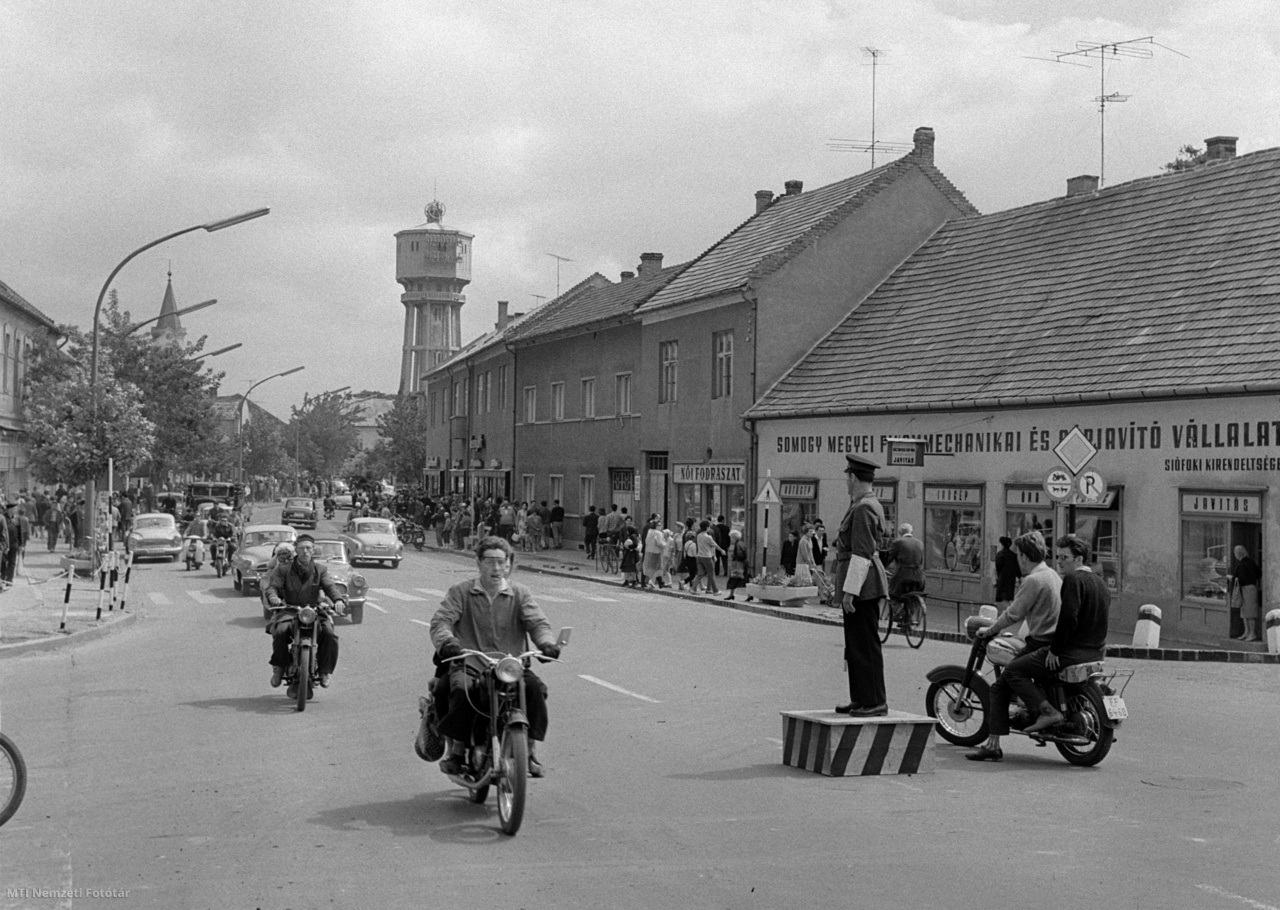 Siófok, 1964. augusztus 6. Rendőr egy dobogón állva irányítja a forgalmat a Balaton-parti város Fő utcáján. A háttérben az 1912-ben Gergely Jenő és Gut Árpád terve alapján készült több mint 40 méter magas víztorony. 
