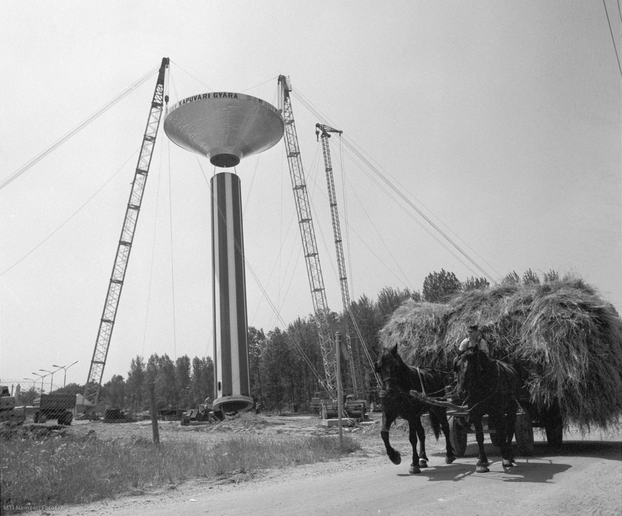 Kapuvár, 1978. június 30. Szénával megrakott lovas kocsi halad a Győr-Sopron megyei Állatforgalmi és Húsipari Vállalat kapuvári gyárának vízellátását szolgáló víztorony mellett, melyet az Építőipari Gépesítő Vállalat szakemberei állítanak fel egy különleges emelőszerkezettel. A hétszáz köbméteres, negyvennyolc méter magas és százharminchat tonna súlyú óriási víztorony a város vízellátásába is besegít majd.