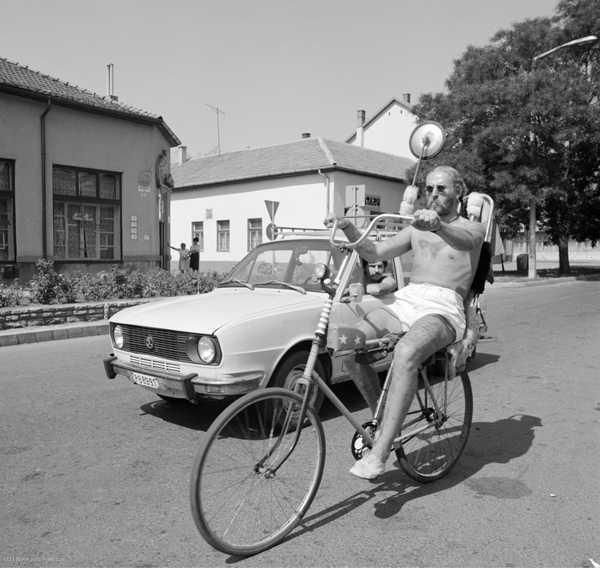 Hatvan, 1983. augusztus 28. Egy Skoda 100-as gépkocsi mellett kerekezik a Kossuth téren magasított kormánnyal és üléstámlával felszerelt kerékpárján egy tetovált, copfos, fölékszerezett férfi, akit általában úgy ismernek: a "hatvani csodabogár".