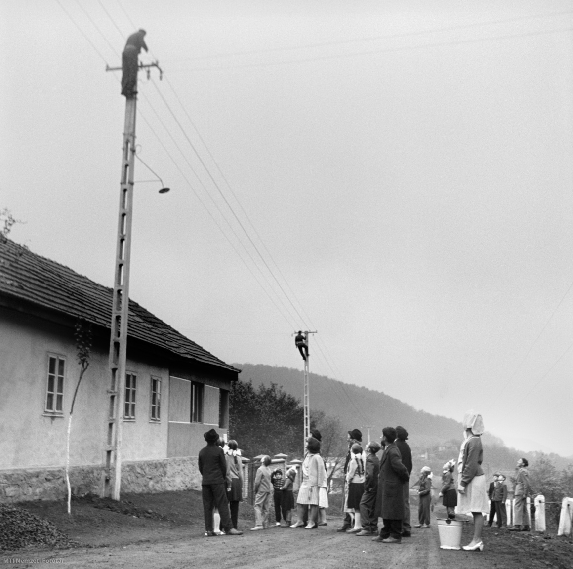 Mátrakeresztes, 1962. november 5. A villanyszerelők munkáját figyelik a település lakói. Az Észak-magyarországi Áramszolgáltató Vállalat salgótarjáni igazgatóságának dolgozói a Magyar Szocialista Munkáspárt (MSZMP) VIII. kongresszusának tiszteletére vállalták, hogy határidő előtt, korábban felgyullad a villanyfény a megye százharmincnyolcadik településén is. A kis mátrai község száznegyven házában és a főutcán is végeztek a munkával, ezzel befejeződött a Nógrád megyei falvak villamosítási programja