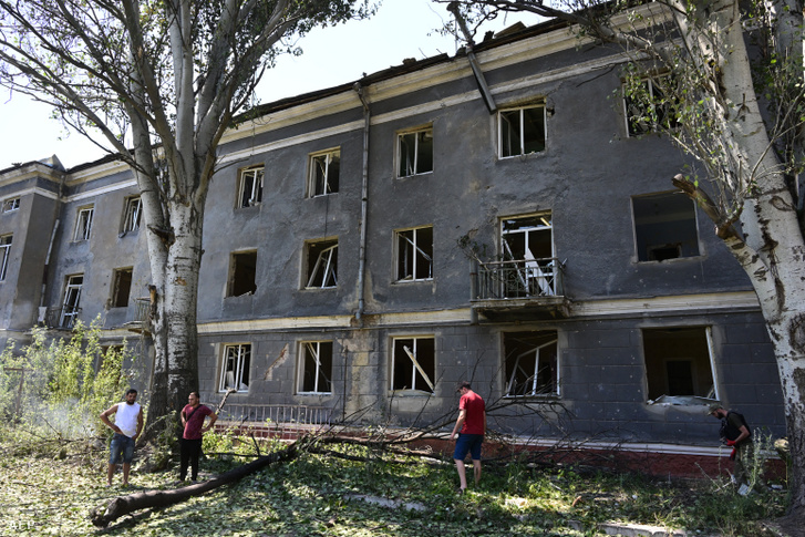 Kramatorszki lakosok állnak egy megsérült épület közelében miután légicsapás ért több lakóházat Kramatorszk központjában 2022. július 7-én