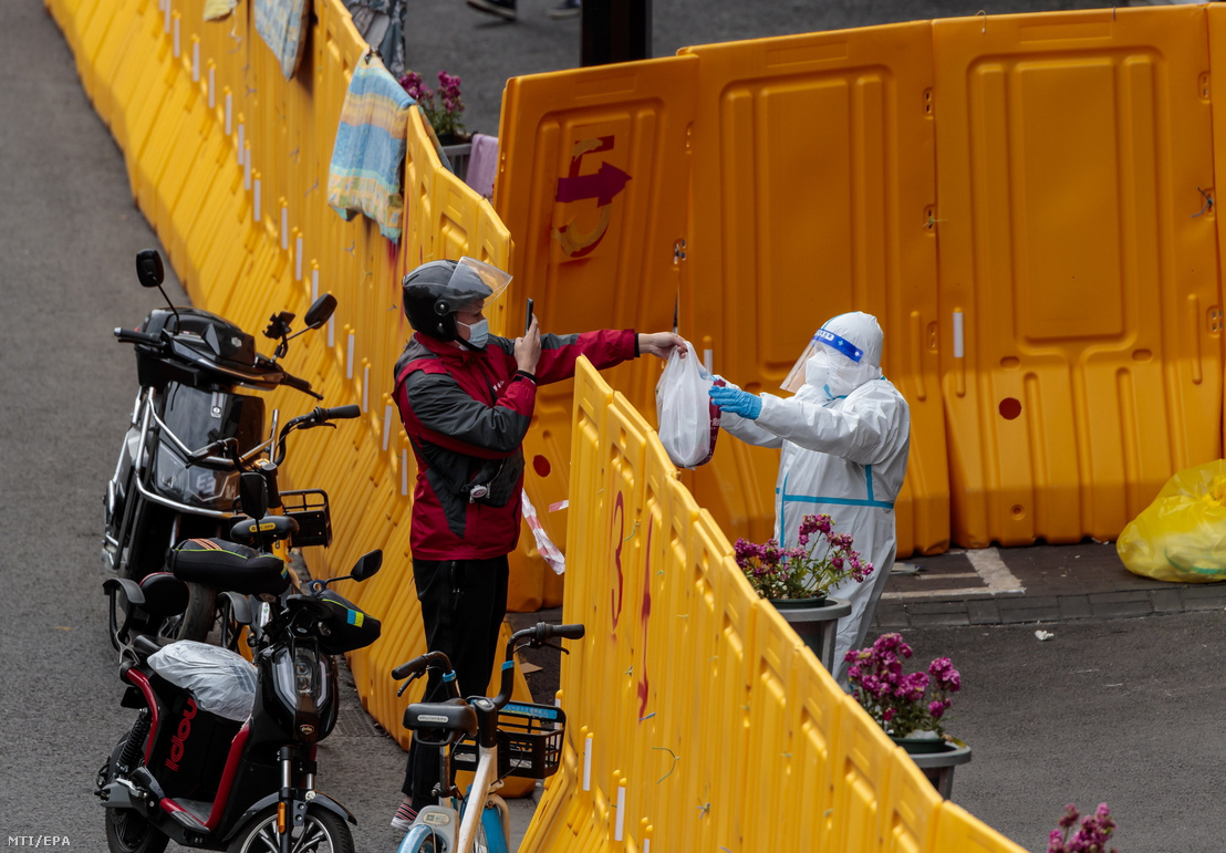Védőruházatot viselő ember átvesz egy csomagot egy futártól a koronavírus-járvány miatt elkerített lakónegyedben Sanghajban 2022. március 28-án