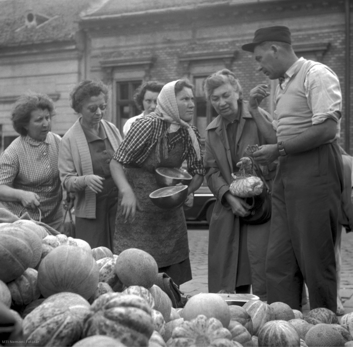 Budapest, 1959. szeptember 1. Egy férfi dinnyét vásárol a Fény utcai piac egyik kofájánál, miközben a többi vevő az árus gyümölcskínálatát szemléli