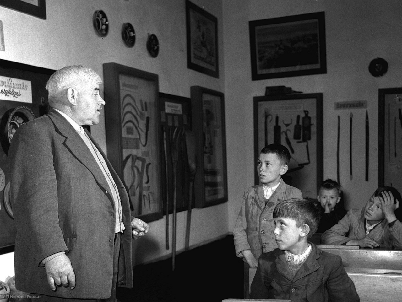 Paszab, 1957. április 22. Turi Sándor 47 esztendeje tanít a paszabi általános iskolában. Mint Móricz Zsigmond barátja, az íróval együtt járta a szatmári falvakat. Falujáró útjai során rengeteg anyagot gyűjtött a paraszti életről, szokásokról. Gyűjtéséből termet rendeztek be a Nyíregyházi Múzeumban, de a paszabi iskolában is őriz az ősi termelőeszközökből és egyéb tárgyakból, amelyek itt szemléltető eszközként szolgálnak. A képen: Turi Sándor tanító Varga Józsefet felelteti, előtérben Balogh Ferenc