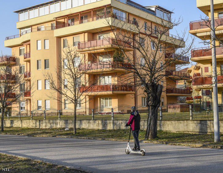 Egy fiatal nő elektromos rollerrel közlekedik egy budapesti lakóparknál 2022. március 26-án
