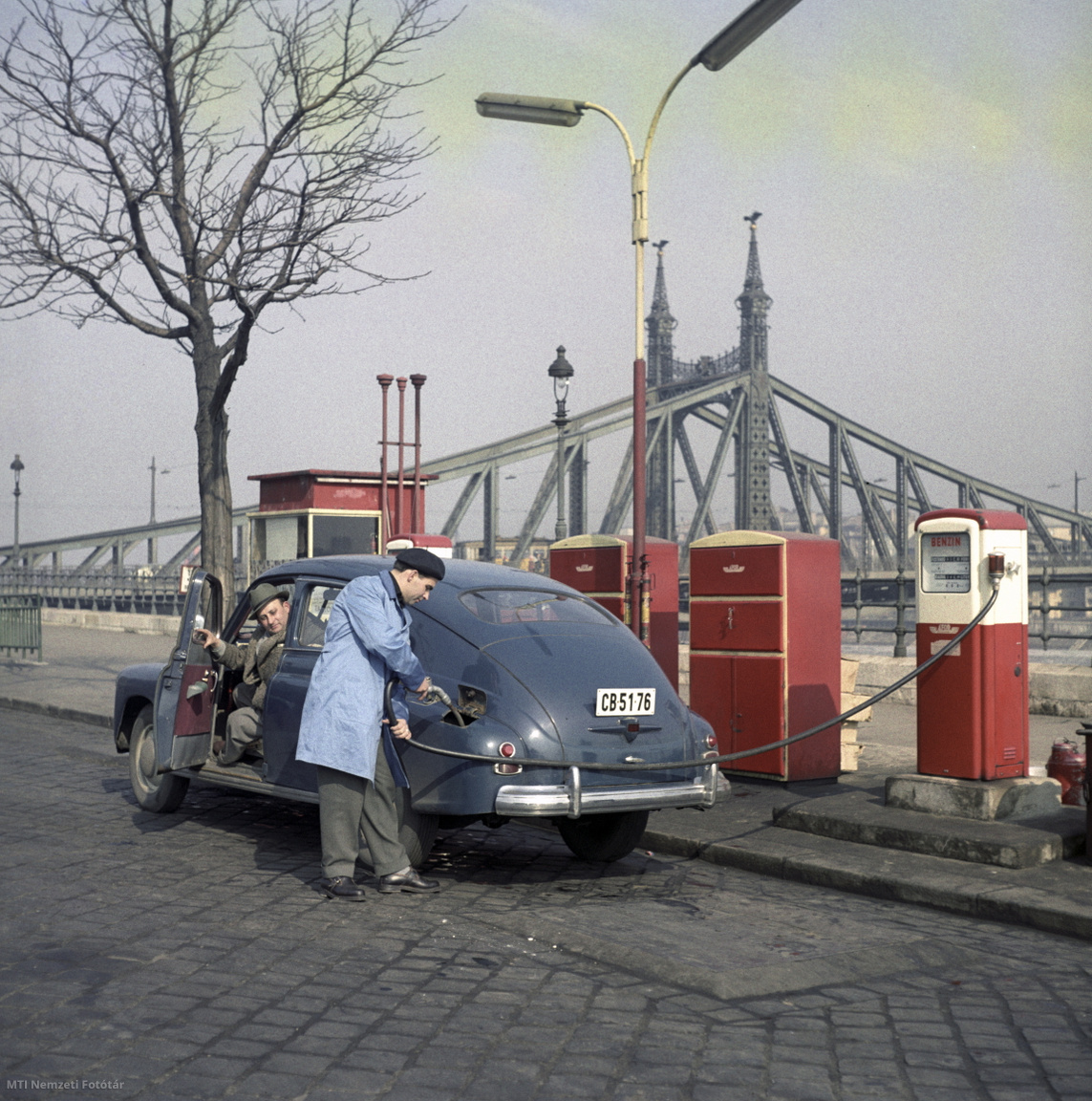 Budapest, 1963. március 4. Az Ásványolaj-forgalmi Vállalat (ÁFOR) üzemanyagtöltő állomásának dolgozója benzint tölt egy GAZ Pobeda típusú autóba a Gellért téri benzinkútnál, a háttérben a Szabadság híd (Fotó: Sziklai Dezső/MTI Nemzeti Fotótár)