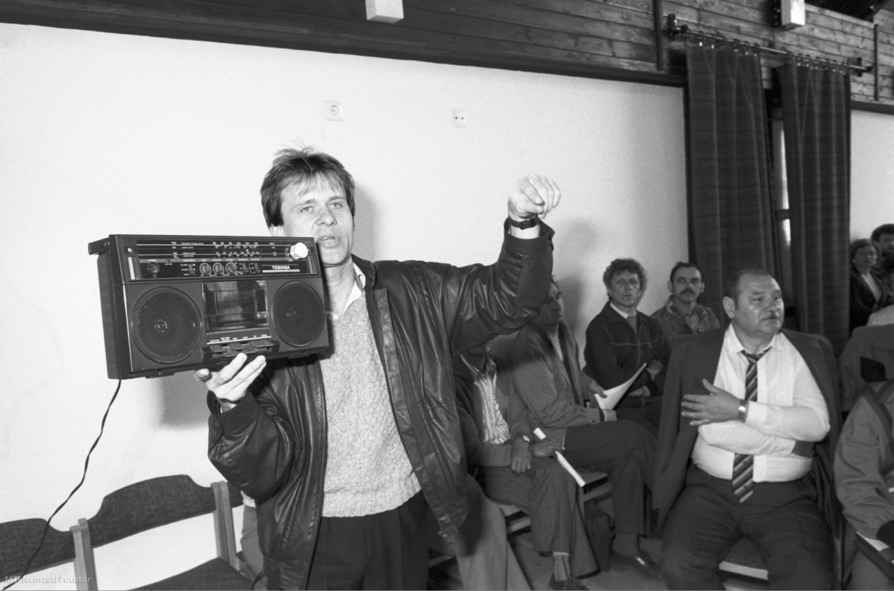 Hatvan, 1989. április 12. Balogh István beszél egy kazettás magnóval a kezében a hatvani Városi Tanács Végrehajtó Bizottságának rendkívüli tanácsülésén a Damjanich Szakmunkásképző Intézet aulájában, hogy tiltakozzanak az autópálya-használati díj bevezetése ellen.